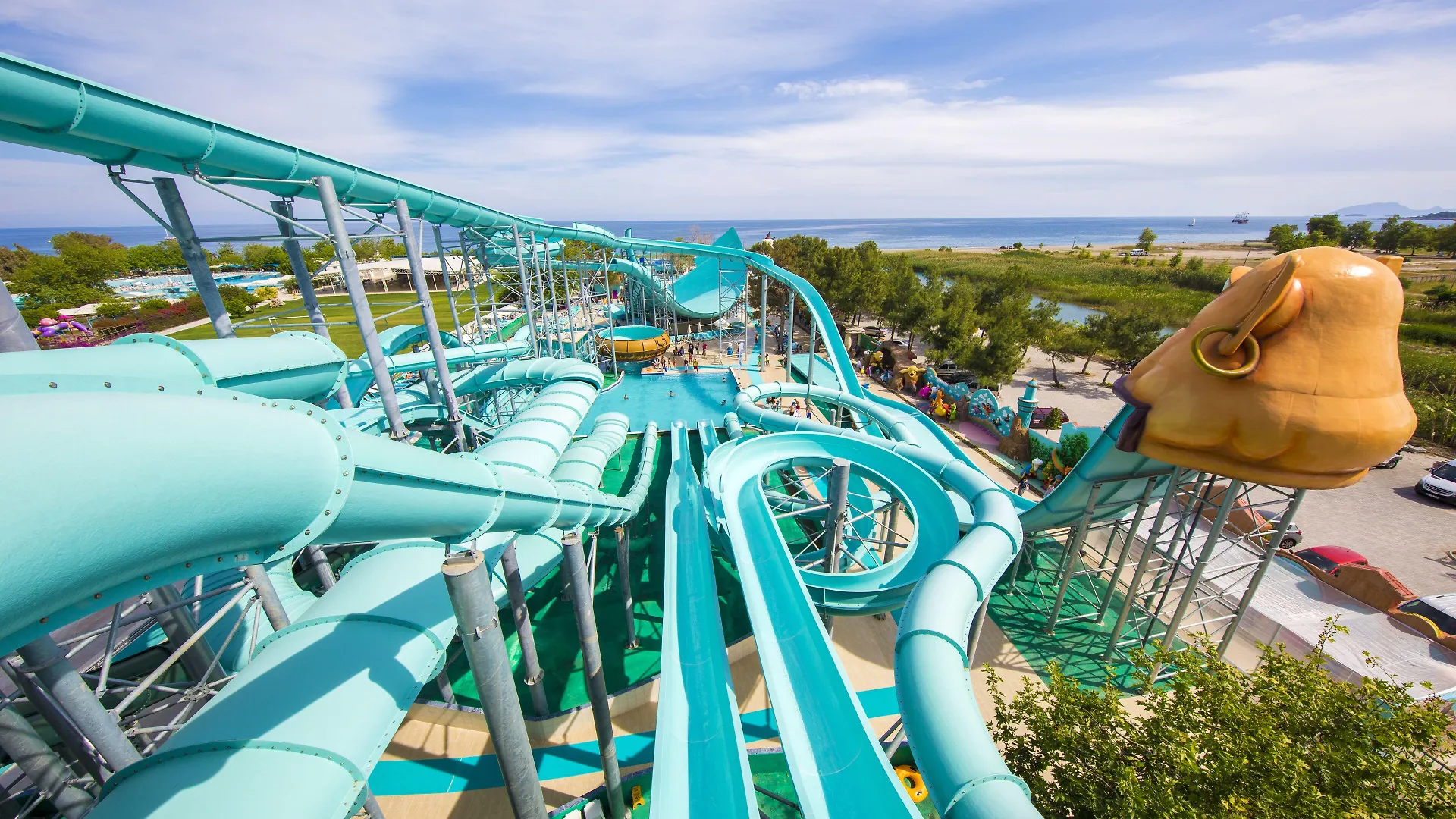 Daima Biz Hotel - Dolusu Aquapark Access Kemer Amenities photo The photo shows a high-angle view of a large, twisting water slide at a water park. The slide is predominantly light blue with some darker blue and green accents, and it features various curves, loops, and drops. 

The slide structure is supported by