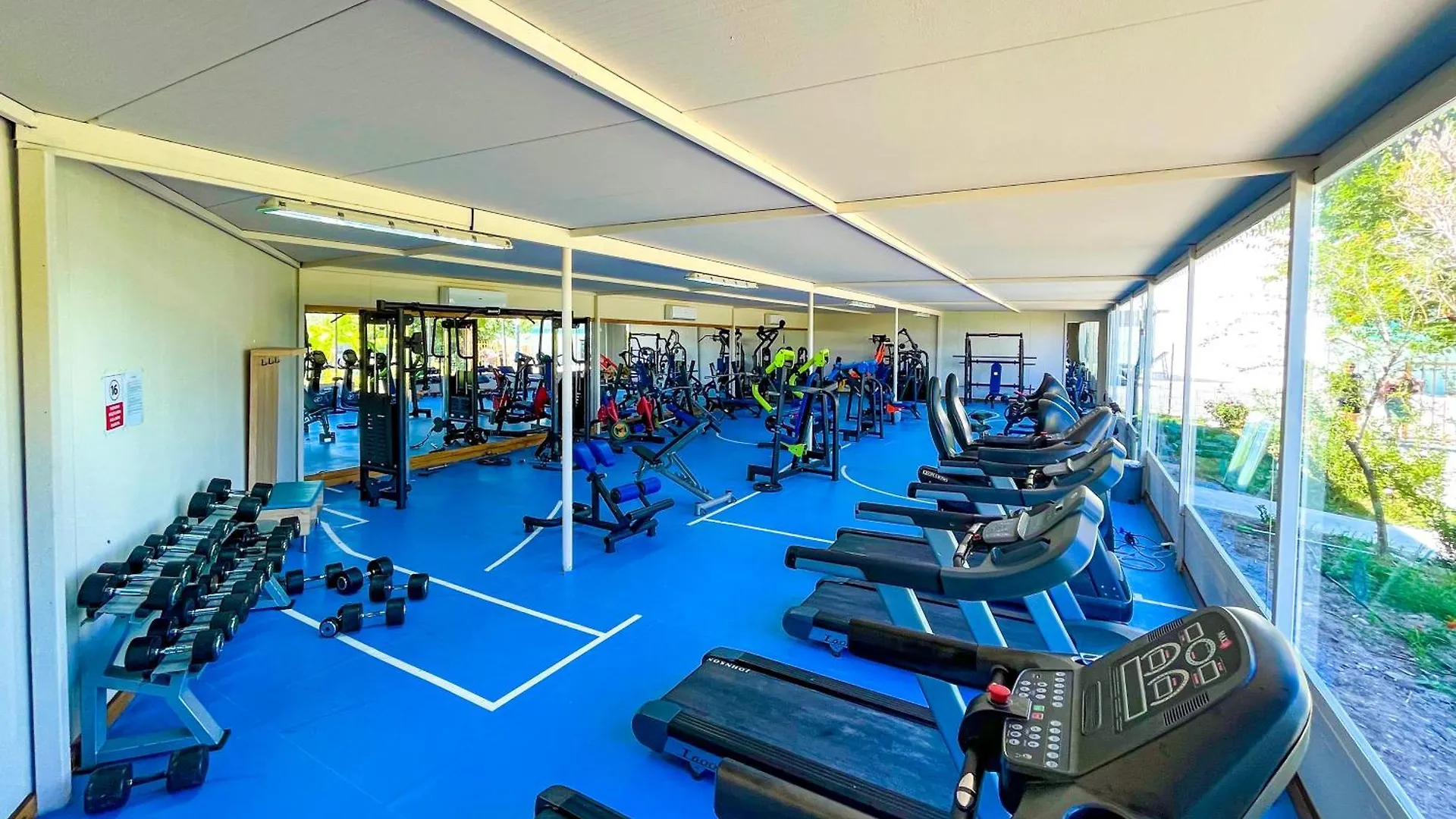 Daima Biz Hotel - Dolusu Aquapark Access Kemer Exterior photo This is a bright, indoor photo of a modern and well-equipped gym or fitness center.

The space is large with a high, light-colored ceiling, and a significant amount of natural light is coming in from large windows along the right side, offering a vie